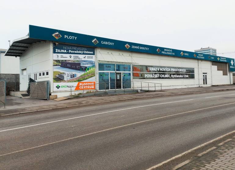 Obchodní prostory na Kamennej ulici v Žilině s reklamními nápisy a prázdným parkovištěm.