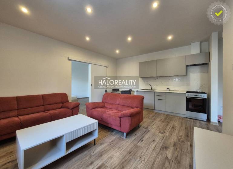 Obývací pokoj v 2-pokojovém bytě s podlahou s dřevěným dekorem, červené sedačky, kuchyně.