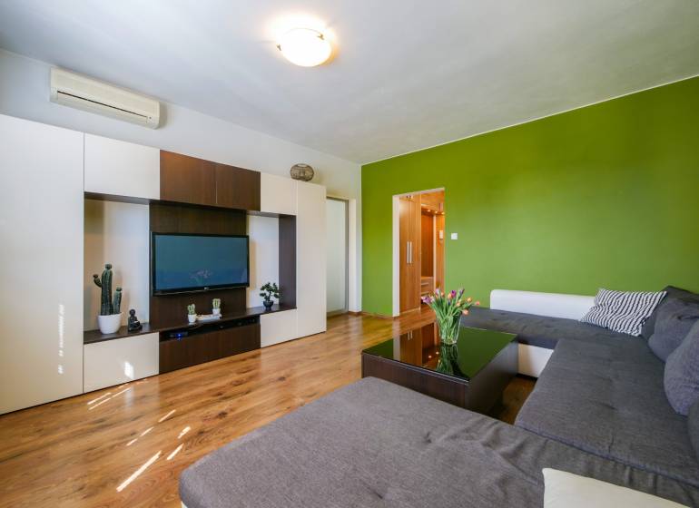 Obývací pokoj ve 3-pokojovém bytě s podlahou s dřevěným dekorem a zelenou stěnou.