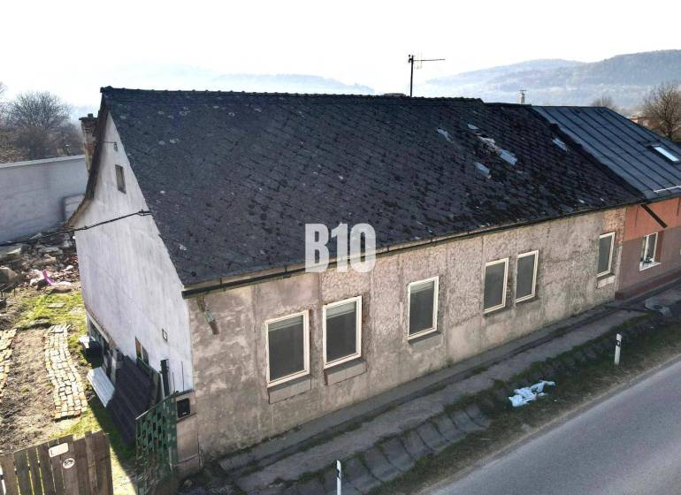 Rodinný dům v Bytči s opotřebovanou střechou a omítkou, vedle hlavní silnice.