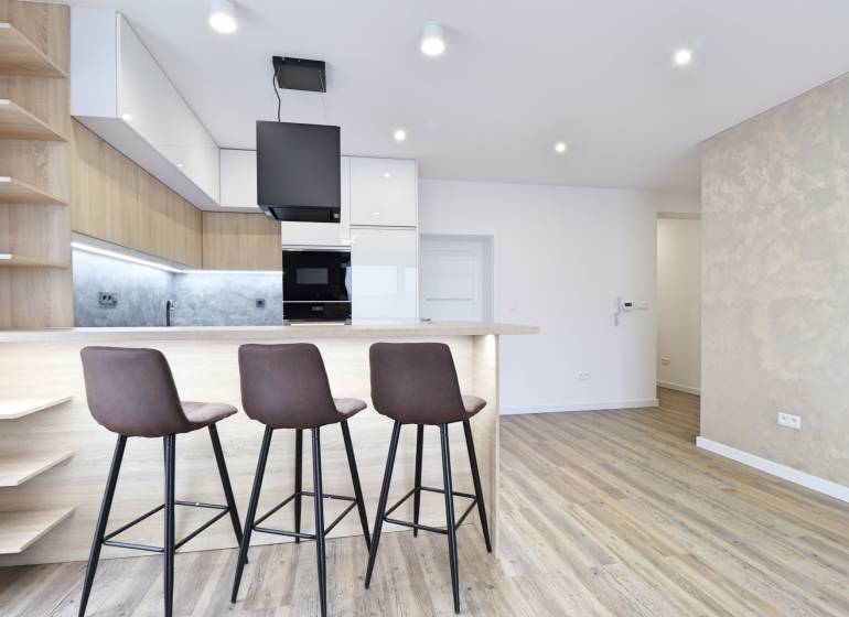 Kuchyně s barovým pultem a podlahou s dřevěným dekorem ve 3pokojovém bytě.