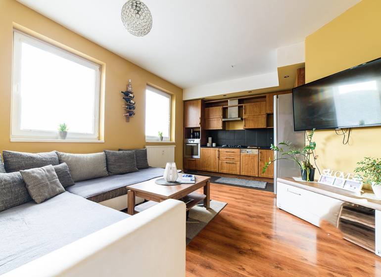 Obývací pokoj v 2-pokojovém bytě s kuchyňským koutem a podlahou s dřevěným dekorem.