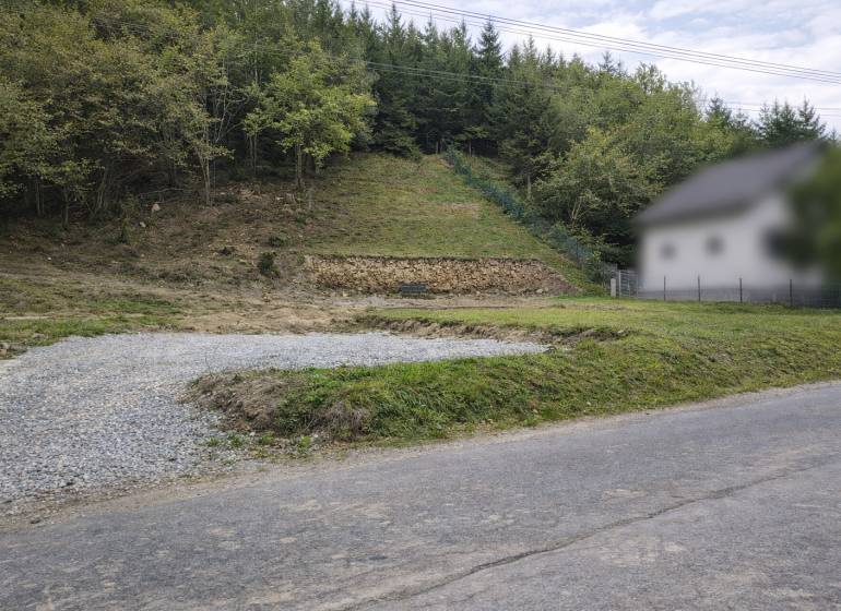 Svažitý pozemek v obci Makov s příjezdovou cestou a okolním lesním porostem. Pozemky - bydlení.