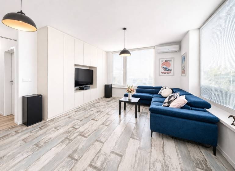 Obývací pokoj v 2-pokojovém bytě s modrou pohovkou a podlahou s dřevěným dekorem.