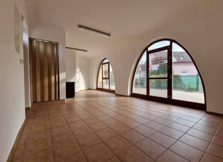 Interiér obchodních prostor s velkými obloukovými okny, dlažba a dřevěné dveře.