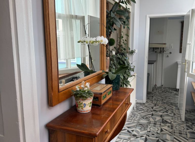 Dřevěná komoda s květinami a zrcadlem, designovaná dlažba na podlaze.
