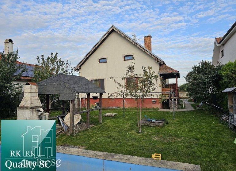 Rodinný dům v Tureni s trávníkem, altánkem a venkovním krbem na zahradě.