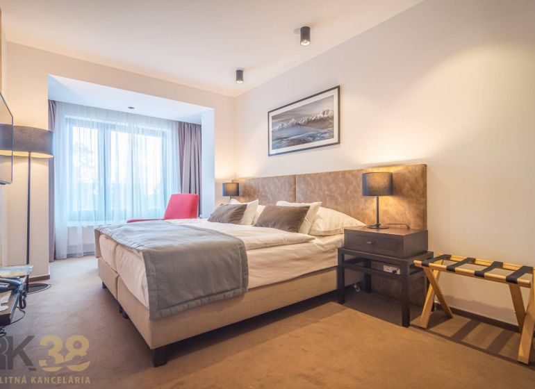 Rekreační apartmán s pohodlnou postelí, červeným křeslem a jemným osvětlením.