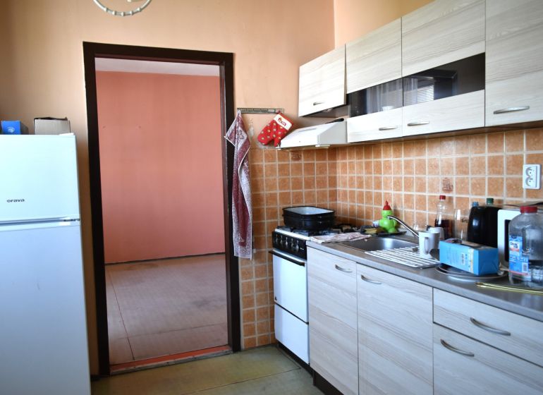 Kuchyně ve 3-pokojovém bytě s dlaždicovým obkladem a podlahou s dřevěným dekorem.
