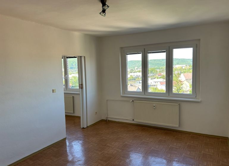 Světlý pokoj se třemi okny a podlahou s dřevěným dekorem v 2pokojovém bytě.