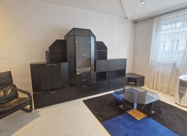 Obývací pokoj s pohovkou, skleněným stolkem a tmavou obývací stěnou ve 3pokojovém bytě.