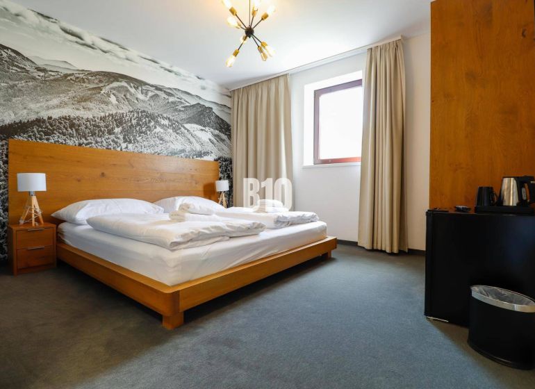 Ložnice v rekreačním apartmánu s dřevěnou postelí a velkoformátovou fotografií krajiny.