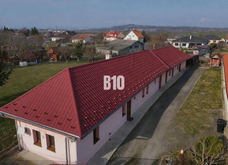 Rodinný dům v Levicích s dlouhou červenou střešní krytinou, obklopený zahradami.