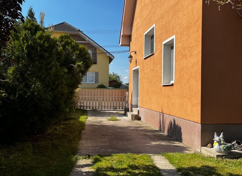 Rodinný dům v Čalovci s oranžovou fasádou, trávníkem a zpevněnou příjezdovou cestou.