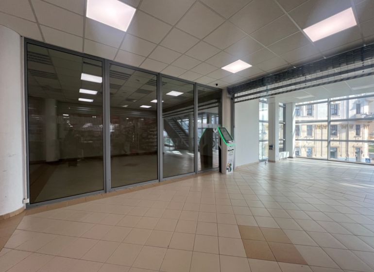 Prosklené obchodní prostory s dlažbou a bankomatem, interiér s velkými okny.