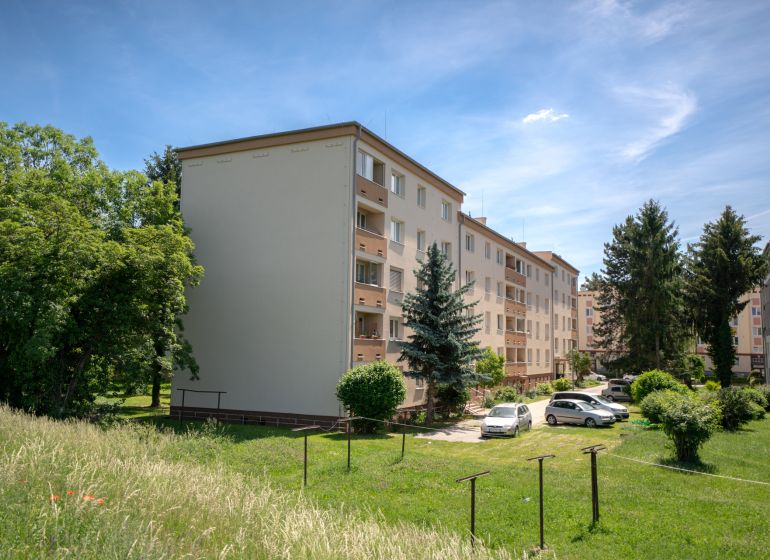 Bytové domy na ulici Švermova v Trenčíně s okolní zelení a zaparkovanými auty.