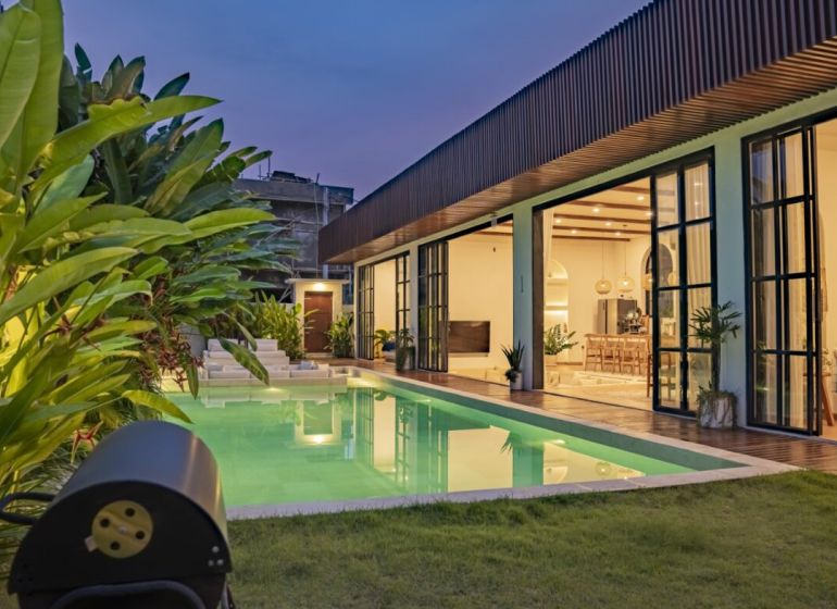 Vila na Bali s osvětleným bazénem, terasou s dřevěným dekorem a zahradou.