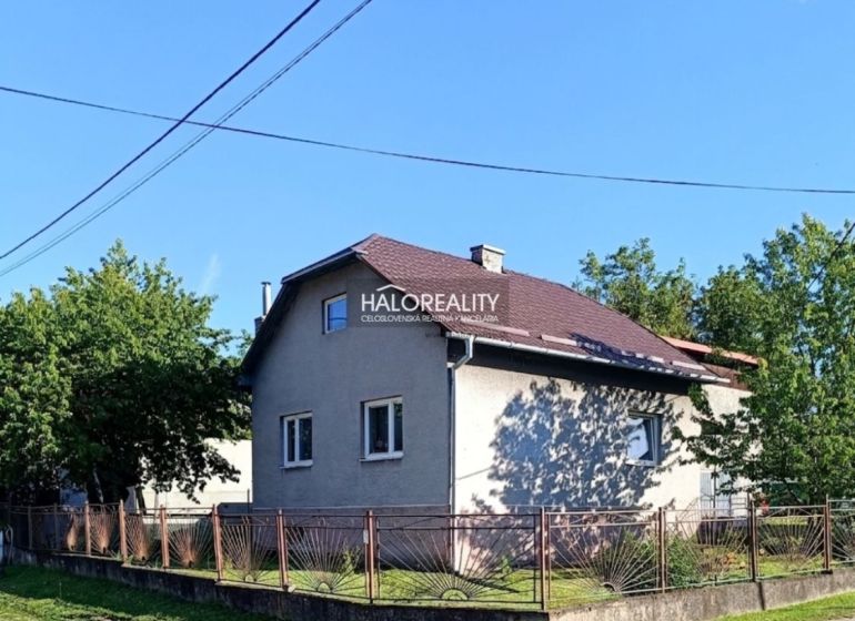 Rodinný dům v Margecanech se šikmou střechou, oplocený, obklopený zelení a modrou oblohou.
