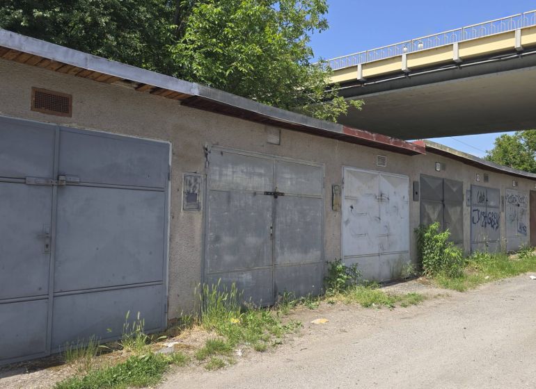 Garáže na Jesenského ulici ve Zvolenu podél cesty se zelení a graffiti.