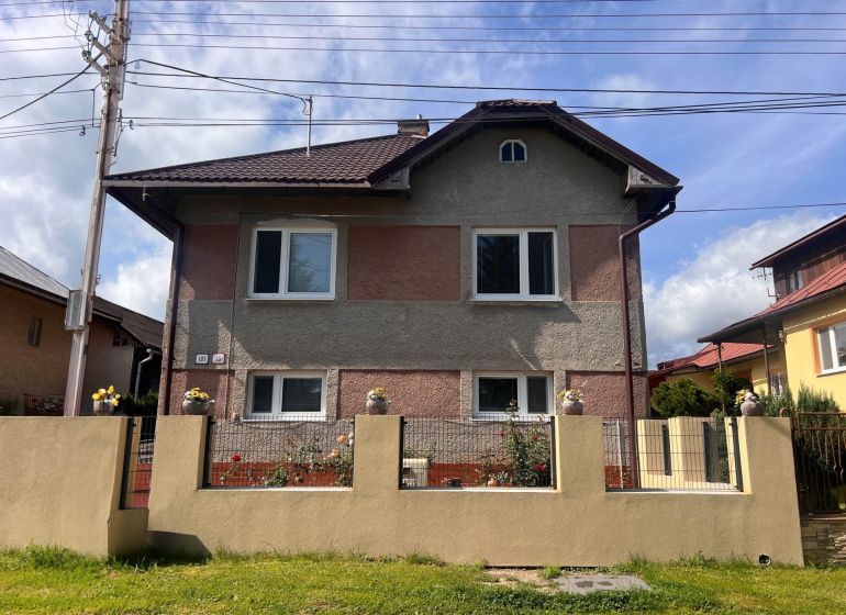 Rodinný dům v Bacúchu obklopený zahradou a oplocením pod modrou oblohou.