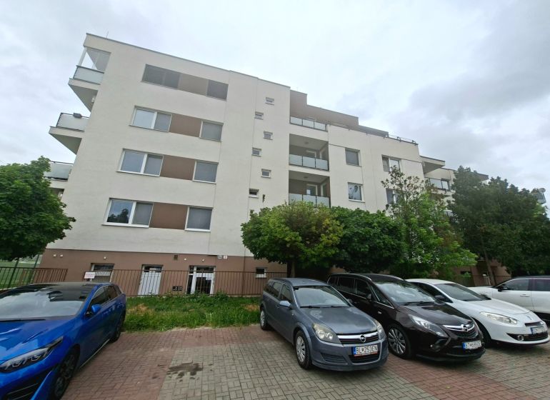 Bytový dům na Športové ulici v Dunajské Lužné s parkovištěm a auty před budovou.