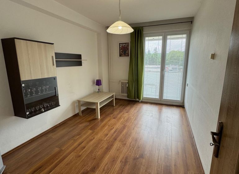 Obývací pokoj v 2pokojovém bytě s podlahou s dřevěným dekorem a balkonem.