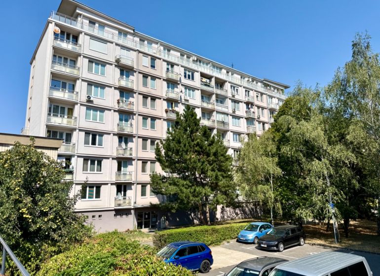 Bytový dům na Piešťanské ulici v Bratislavě - Nové Město obklopený zelení a parkovištěm.