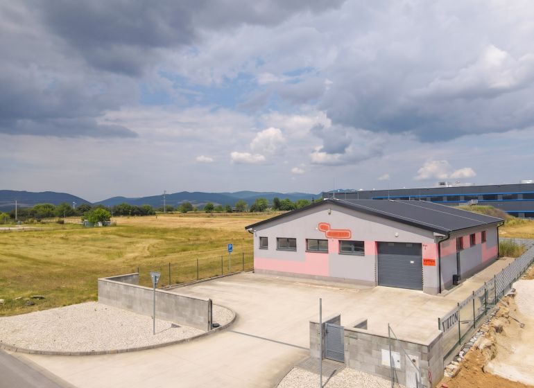 Průmyslová stavba v Nové Dubnici obklopená poli a horami.