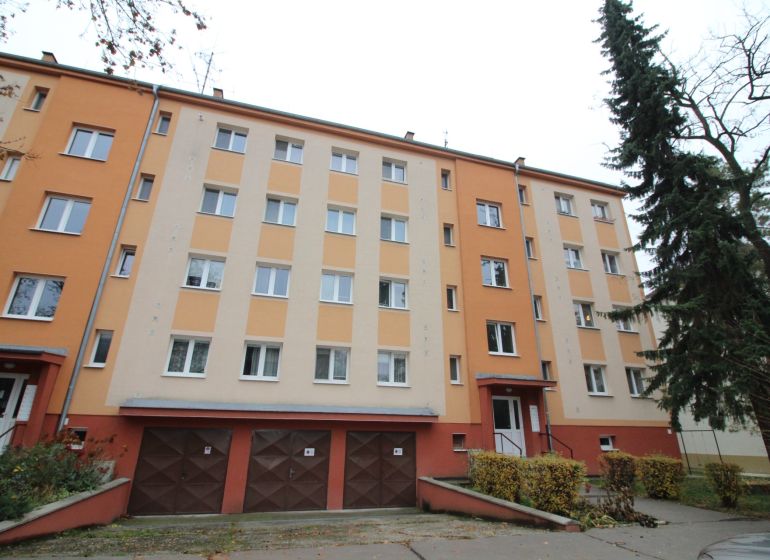 Bytový dům v Trnavě s barevnou fasádou, garážemi a okolím se stromy.