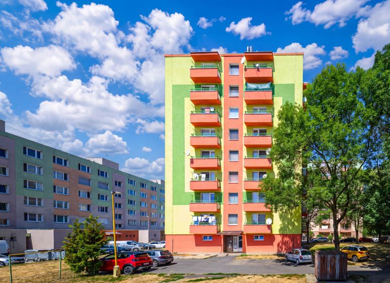 Barevné bytové domy na Sládkovičově ulici ve Fiľakovu s parkovištěm a zelení.