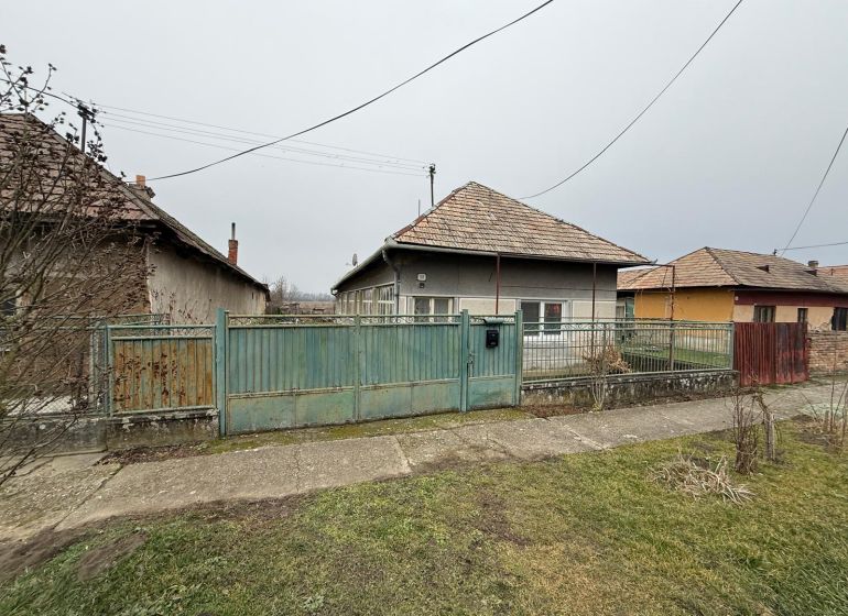 Rodinný dům v Sikenici se starším plotem a zahradou, obklopený dalšími domy.