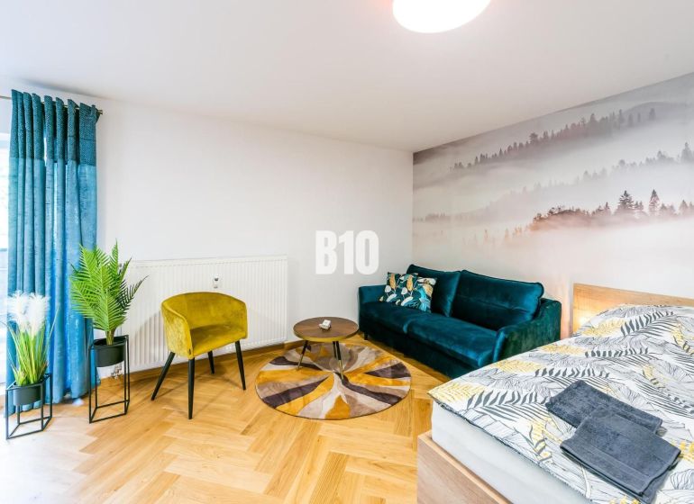 Stylový rekreační apartmán s podlahou s dřevěným dekorem, pohovkou a rostlinami.