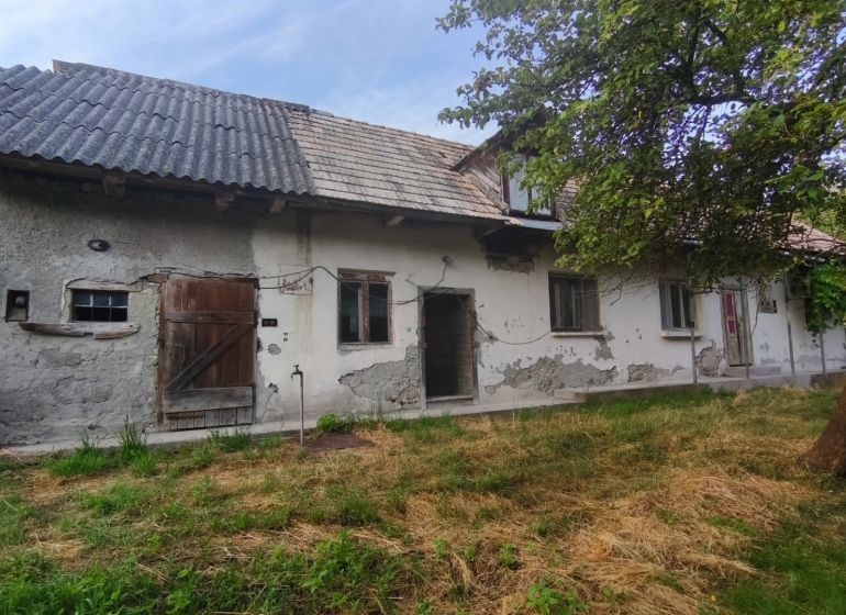 Rodinný dům v Čelovcích s opotřebovanou omítkou, dřevěnými dveřmi a zahradou.