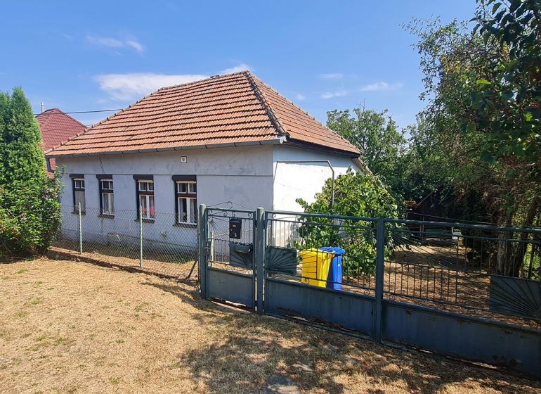 Rodinný dům v Dolních Otrokovicích s plotem a zahradou na slunném pozemku.