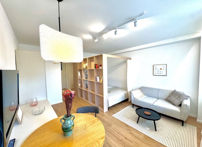 Obývací pokoj s podlahou s dřevěným dekorem, světlou pohovkou a jídelním stolem v 1-pokojovém bytě.