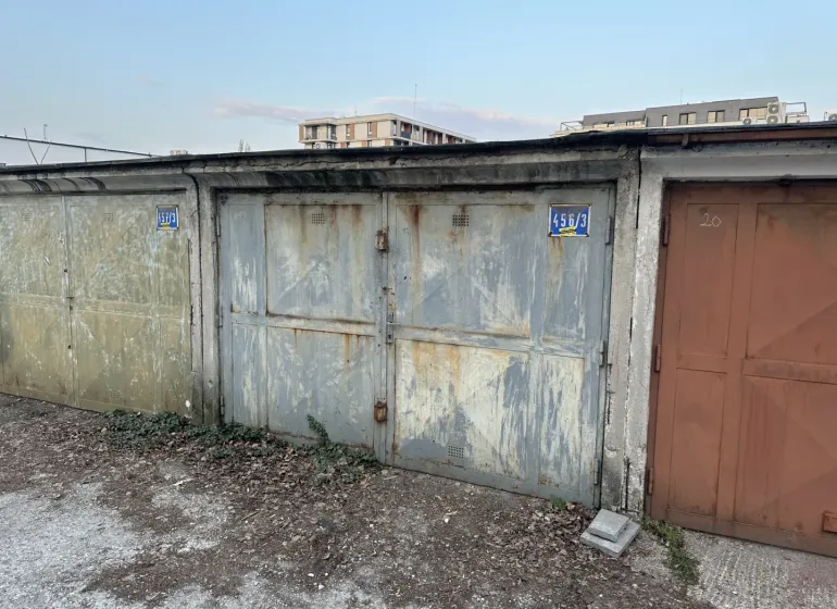 Opuštěné garáže v Bratislavě - Novém Městě s opadanou omítkou a plechovými dveřmi.
