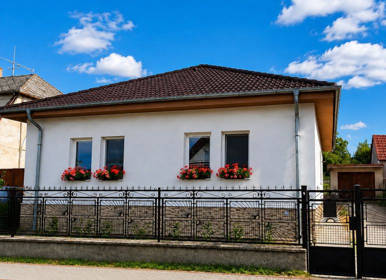 Rodinný dům v Šalgočce s bílou fasádou, okenními květinami a valbovou střechou.
