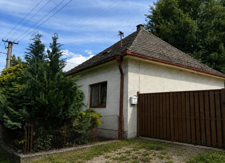 Rodinný dům v Urmincích na ulici Klačany, obklopený dřevinami a plotem.