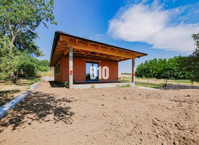 Rodinný dům v Čeľadiciach s nedokončenou zahradou, obklopený zelení a modrou oblohou.