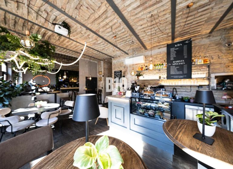 Stylové gastro prostory s cihlovými klenbami, zelení a podlahou s dřevěným dekorem.