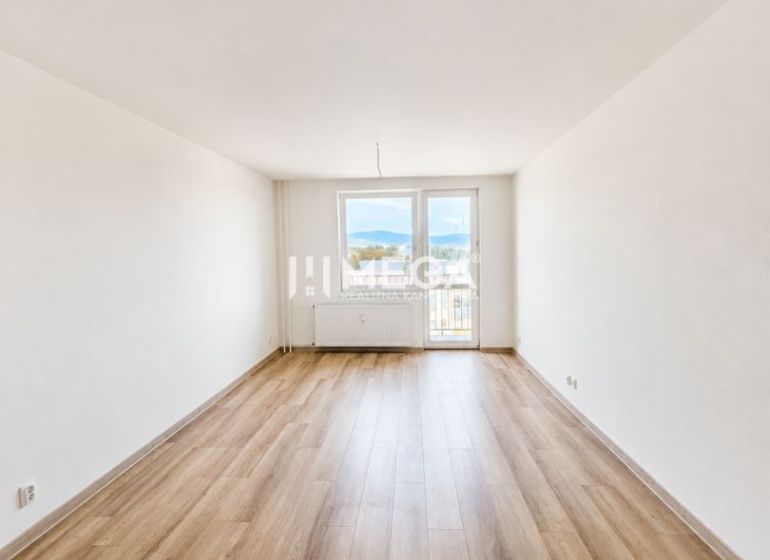 Prostorný obývací pokoj se vstupem na balkon a podlahou s dřevěným dekorem v 2pokojovém bytě.