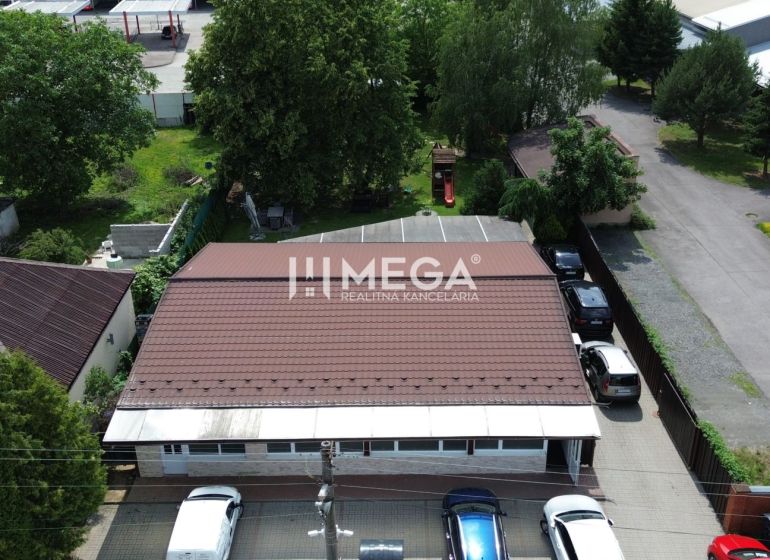 Gastro prostory na Budovatelské ulici ve Vranově nad Topľou obklopené auty a zelení.