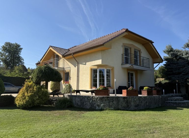 Rodinný dům ve Zlatých Moravcích, obklopený zelení, s kamennou terasou a balkónem.