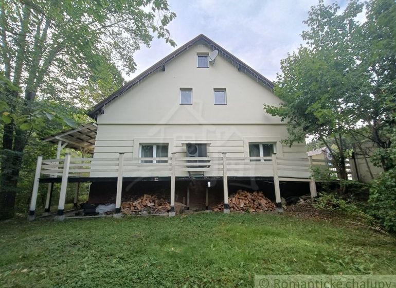 Rodinný dům ve Staškově, obklopený zelení, s dřevem uskladněným pod terasou.