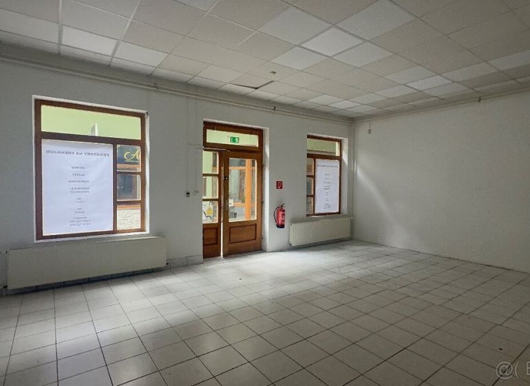Obchodní prostory s dlažbou a velkými okny, čekající na využití.