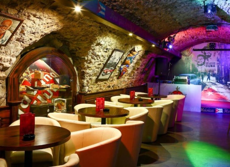 Bar v historických gastro prostorech s kamennými stěnami a podlahou s dřevěným dekorem.
