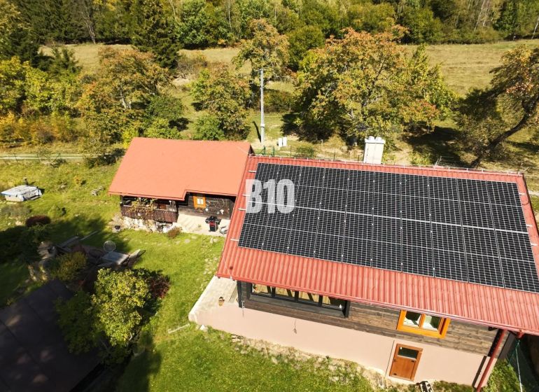 Dřevěná chata v Dlouhém Poli se solárními panely, obklopená zelení a přírodou.