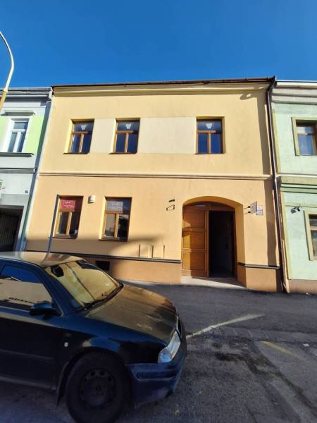 Budova s okny a vchodem v Prešově na Slovenské ulici, před ní zaparkované auto.