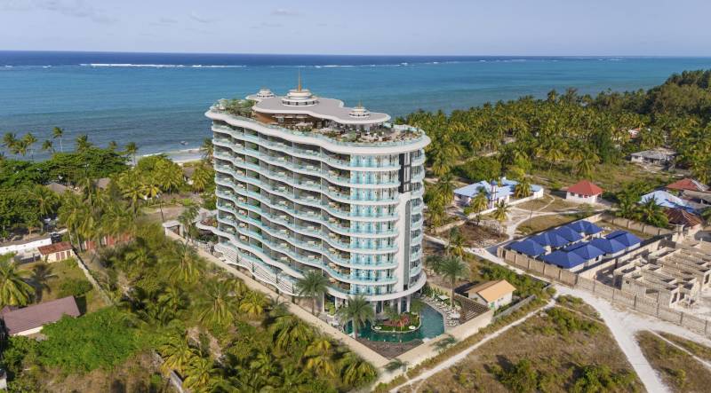 Apartmánový komplex u pláže v Paje s výhledem na oceán a palmovými stromy.