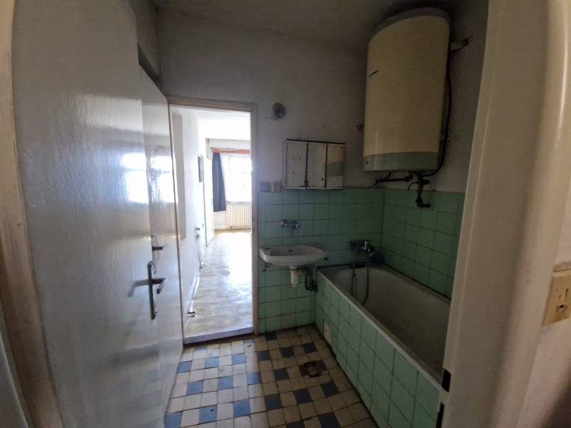 Koupelna s vanou, umyvadlem a starším bojlerem v rodinném domě.